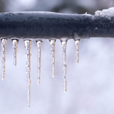Frozen icicles on a gray pipe after a thaw in winter. Background. Form.